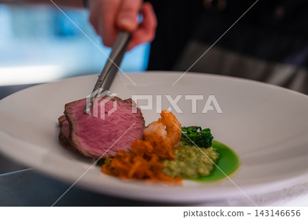 A chef uses tweezers to place medium rare beef beside a prawn, braised vegetables, green puree, and herb sauce at a luxury hotel restaurant in Oberlech, Austria. A chef uses tweezers to place medium rare beef beside a prawn, braised vegetables, green puree, and herb sauce at a luxury hotel restaurant in Oberlech, Austria. 143146656