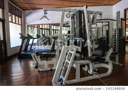 Daytime resort gym in Maldives shows multi station machine, treadmills, and free weights with mirrors, wood floors, high ceilings, and windows to tropical plants. Daytime resort gym in Maldives shows multi station machine, treadmills, and free weights with mirrors, wood floors, high ceilings, and windows to tropical plants. 143146684