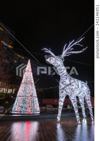 A reindeer sculpture and lace like cone tree glow in a Liverpool plaza at night, reflections on wet paving near modern apartments, long exposure and cool pastel lights A reindeer sculpture and lace like cone tree glow in a Liverpool plaza at night, reflections on wet paving near modern apartments, long exposure and cool pastel lights 143146951