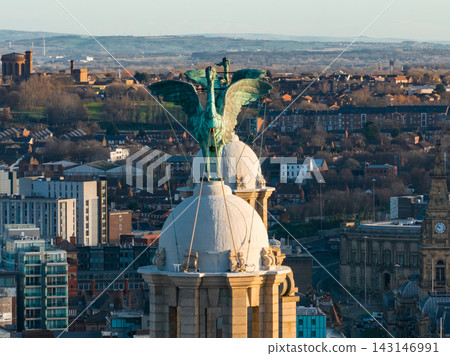 Aerial close up shows Liver Bird atop Royal Liver Building in Liverpool at sunrise. Verdigris copper, cables, ornate stonework, rooftops, clock towers, housing, and glass blocks. Aerial close up shows Liver Bird atop Royal Liver Building in Liverpool at sunrise. Verdigris copper, cables, ornate stonework, rooftops, clock towers, housing, and glass blocks. 143146991