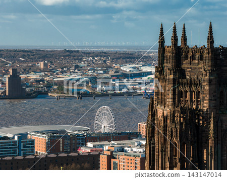 High angle view over Liverpool, UK shows River Mersey, Liverpool Cathedral, Albert Dock Ferris wheel, arena roof, and offshore wind turbines at sunrise. 143147014