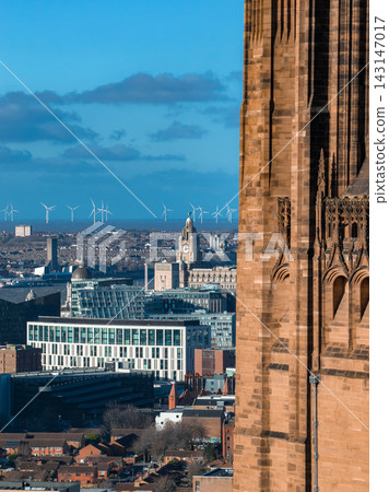 Aerial sunrise view of Liverpool shows Liverpool Cathedral on the right, modern and historic buildings, the Royal Liver Building clock tower, and wind turbines beyond the River Mersey. Aerial sunrise view of Liverpool shows Liverpool Cathedral on the right, modern and historic buildings, the Royal Liver Building clock tower, and wind turbines beyond the River Mersey. 143147017