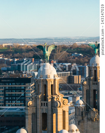 Aerial view of Liverpool, UK, with twin clock tower domes and green copper Liver Birds. Warm low angle light gilds sandstone, modern offices, red brick, and distant hills. Aerial view of Liverpool, UK, with twin clock tower domes and green copper Liver Birds. Warm low angle light gilds sandstone, modern offices, red brick, and distant hills. 143147019