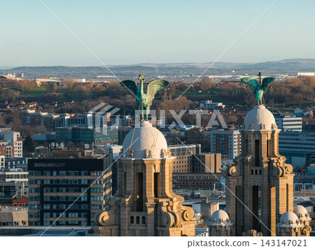 Aerial sunrise view in central Liverpool shows the Royal Liver Building twin towers with Liver Bird statues, warm light on pale stone, city blocks, and distant hills. Aerial sunrise view in central Liverpool shows the Royal Liver Building twin towers with Liver Bird statues, warm light on pale stone, city blocks, and distant hills. 143147021