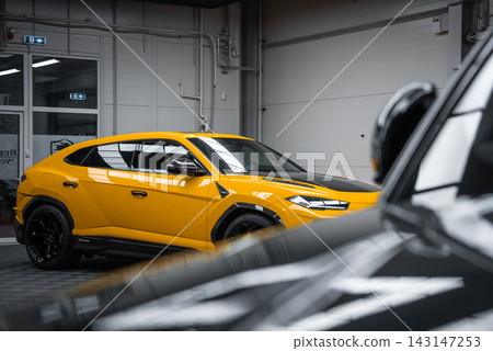 A yellow Lamborghini Urus Performante sits in a showroom garage, three quarter side view, soft studio lighting, carbon accents, large black wheels, razor edged LED headlights. A yellow Lamborghini Urus Performante sits in a showroom garage, three quarter side view, soft studio lighting, carbon accents, large black wheels, razor edged LED headlights. 143147253