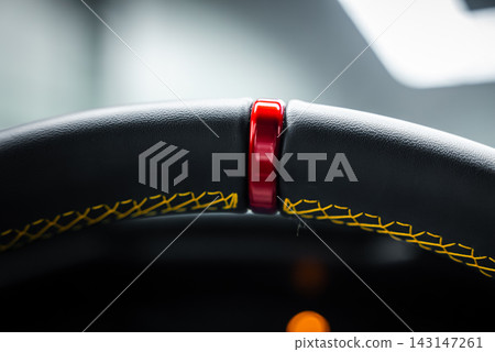 Close up macro shows a steering wheel red center marker at 12, thick black leather rim, bold yellow cross stitching, soft light, and an amber dash glow. Close up macro shows a steering wheel red center marker at 12, thick black leather rim, bold yellow cross stitching, soft light, and an amber dash glow. 143147261