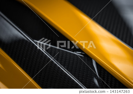 Close up shows yellow bodywork, exposed carbon fiber, and gloss black trim on a Lamborghini Urus Performante. Soft diffused light highlights textures and precise lines. Close up shows yellow bodywork, exposed carbon fiber, and gloss black trim on a Lamborghini Urus Performante. Soft diffused light highlights textures and precise lines. 143147263