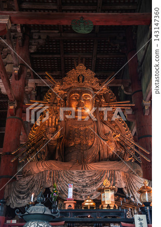 A gilded Buddhist statue sits in a wooden hall in Nara, Japan. Warm light reveals carved halo spines, layered robes, dark beams, and a coffered ceiling in a calm setting. A gilded Buddhist statue sits in a wooden hall in Nara, Japan. Warm light reveals carved halo spines, layered robes, dark beams, and a coffered ceiling in a calm setting. 143147360