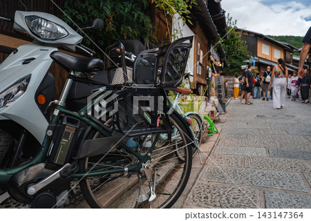 A low angle street scene in Kyoto Higashiyama shows a parked electric bicycle and a white scooter by wooden buildings and stone lanes, with pedestrians in soft blur. A low angle street scene in Kyoto Higashiyama shows a parked electric bicycle and a white scooter by wooden buildings and stone lanes, with pedestrians in soft blur. 143147364