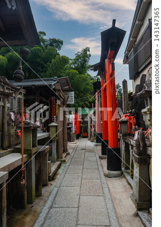 Granite lanterns, fox statues with red bibs, and miniature torii line a stone path at Fushimi Inari Taisha in Kyoto, Japan, in soft afternoon light with bamboo behind. Granite lanterns, fox statues with red bibs, and miniature torii line a stone path at Fushimi Inari Taisha in Kyoto, Japan, in soft afternoon light with bamboo behind. 143147365