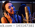 Smiling woman wearing headphones and singing while looking at camera 143147381