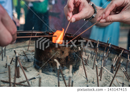 Close up hands light slender incense sticks at a shrine in Nara, Japan. Warm flames, ash, and spent sticks show ritual practice as soft daylight frames a candid moment. Close up hands light slender incense sticks at a shrine in Nara, Japan. Warm flames, ash, and spent sticks show ritual practice as soft daylight frames a candid moment. 143147415