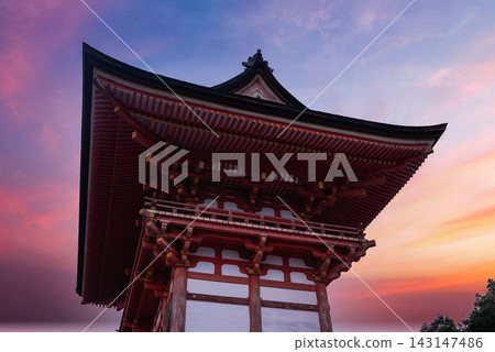 Low angle view of a red wooden temple gate in Kyoto at dusk, pagoda eaves and timber joinery stand out as the sunset colors frame the historic shrine entrance. Low angle view of a red wooden temple gate in Kyoto at dusk, pagoda eaves and timber joinery stand out as the sunset colors frame the historic shrine entrance. 143147486