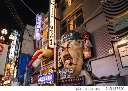 Night in Dotonbori Osaka shows an oversized chef head gripping sushi, neon kanji signs, tall narrow buildings, and crowded shopfronts in warm contrasty light. Night in Dotonbori Osaka shows an oversized chef head gripping sushi, neon kanji signs, tall narrow buildings, and crowded shopfronts in warm contrasty light. 143147801