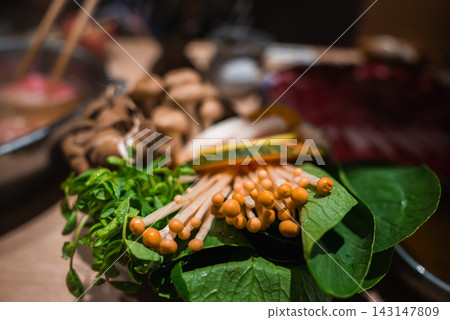Close up of enoki mushrooms and leafy greens on a wooden platter in Osaka, Japan. Warm light and shallow depth highlight textures for shabu shabu or sukiyaki. Close up of enoki mushrooms and leafy greens on a wooden platter in Osaka, Japan. Warm light and shallow depth highlight textures for shabu shabu or sukiyaki. 143147809