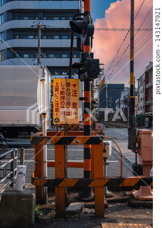 Street level view in Osaka shows a railway crossing with black and orange barriers, signal lights, and a truck passing, late afternoon light adds a warm cinematic mood. Street level view in Osaka shows a railway crossing with black and orange barriers, signal lights, and a truck passing, late afternoon light adds a warm cinematic mood. 143147921