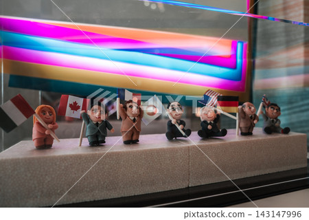 Seven handcrafted figurines sit in a row holding flags of Indonesia, Canada, Japan, and the United States in a museum exhibit in Hiroshima with a neon style backdrop. Seven handcrafted figurines sit in a row holding flags of Indonesia, Canada, Japan, and the United States in a museum exhibit in Hiroshima with a neon style backdrop. 143147996