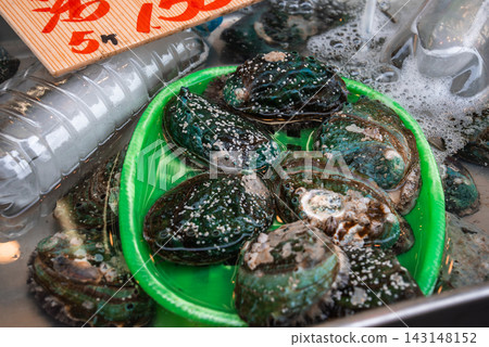 A green tray holds live abalones in a shallow market tank, shells wet with foam and salt, a red price sign above at a Tokyo stall, travel and food culture on display. A green tray holds live abalones in a shallow market tank, shells wet with foam and salt, a red price sign above at a Tokyo stall, travel and food culture on display. 143148152