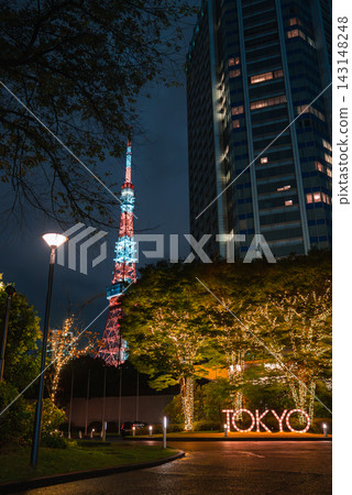 Night scene in Tokyo, with Tokyo Tower behind a high rise, trees wrapped in warm lights along a walkway, and a glowing TOKYO sign at a plaza in Minato. Night scene in Tokyo, with Tokyo Tower behind a high rise, trees wrapped in warm lights along a walkway, and a glowing TOKYO sign at a plaza in Minato. 143148248