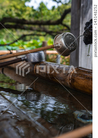 Close view of a temizuya at a Tokyo Shinto shrine shows a dragon spout, water drops, bamboo troughs, and metal ladles resting on wood in soft light. Close view of a temizuya at a Tokyo Shinto shrine shows a dragon spout, water drops, bamboo troughs, and metal ladles resting on wood in soft light. 143148252