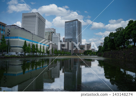 Daytime view in central Tokyo shows a canal reflecting glass towers near the Marunouchi district and the Imperial Palace moat, with trees and stone embankment in frame. Daytime view in central Tokyo shows a canal reflecting glass towers near the Marunouchi district and the Imperial Palace moat, with trees and stone embankment in frame. 143148274
