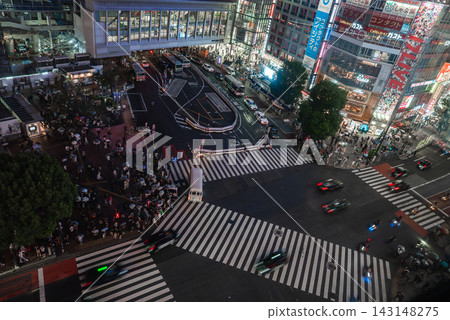 Aerial view shows Shibuya Crossing at night in Tokyo, neon billboards, diagonal zebra lines, buses and taxis loop near Shibuya Station as crowds wait to cross. Aerial view shows Shibuya Crossing at night in Tokyo, neon billboards, diagonal zebra lines, buses and taxis loop near Shibuya Station as crowds wait to cross. 143148275