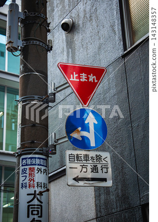 Japanese stop, direction, and one way except bicycles signs mount on a utility pole in Tokyo. Glass offices and concrete building set the urban scene with light traffic. Japanese stop, direction, and one way except bicycles signs mount on a utility pole in Tokyo. Glass offices and concrete building set the urban scene with light traffic. 143148357