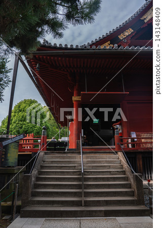 Stone steps rise to a deep red wooden hall at Senso ji in Asakusa, Tokyo, with lanterns, lattice details, eaves, and crimson pillars under a green tree canopy. Stone steps rise to a deep red wooden hall at Senso ji in Asakusa, Tokyo, with lanterns, lattice details, eaves, and crimson pillars under a green tree canopy. 143148409
