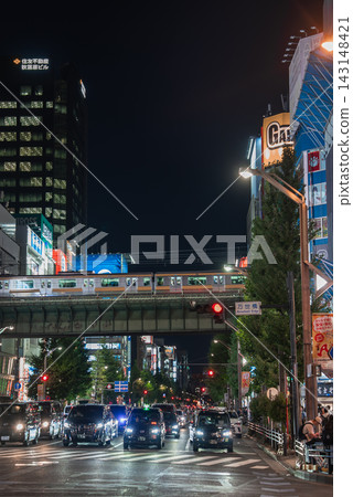 A green JR Yamanote Line train passes an elevated track as cars wait at a red light below in Tokyo, neon signs and office towers glow, crowds fill sidewalks. A green JR Yamanote Line train passes an elevated track as cars wait at a red light below in Tokyo, neon signs and office towers glow, crowds fill sidewalks. 143148421