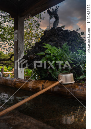A temizuya at a Tokyo shrine shows a coiled dragon spout pouring into a bamboo trough, a wooden ladle on the rim, and a small pavilion with garden leaves in view. A temizuya at a Tokyo shrine shows a coiled dragon spout pouring into a bamboo trough, a wooden ladle on the rim, and a small pavilion with garden leaves in view. 143148431