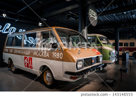White and gold RAF 2203 Latvija with Moskva 1980 torch emblem stands in front, green and cream microbus behind, cool spotlights, signage, reflective finishes present White and gold RAF 2203 Latvija with Moskva 1980 torch emblem stands in front, green and cream microbus behind, cool spotlights, signage, reflective finishes present 143148553