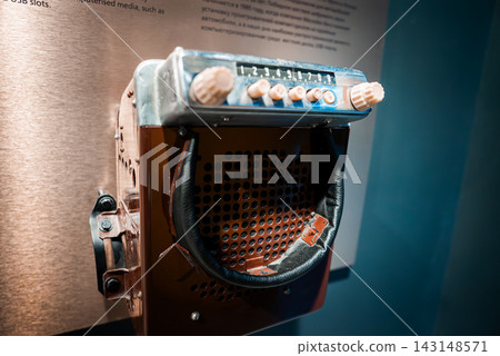 Close up of a chrome car radio with buttons 1 to 6, large tuning knobs, and perforated speaker with worn leather strap, mounted on a wall in a museum display. Close up of a chrome car radio with buttons 1 to 6, large tuning knobs, and perforated speaker with worn leather strap, mounted on a wall in a museum display. 143148571