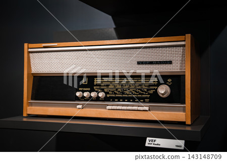 Close up of a wooden VEF Radio 1965 on a dark museum shelf, with silver mesh grille, Cyrillic station markers, white knobs, and tight studio style composition. Close up of a wooden VEF Radio 1965 on a dark museum shelf, with silver mesh grille, Cyrillic station markers, white knobs, and tight studio style composition. 143148709