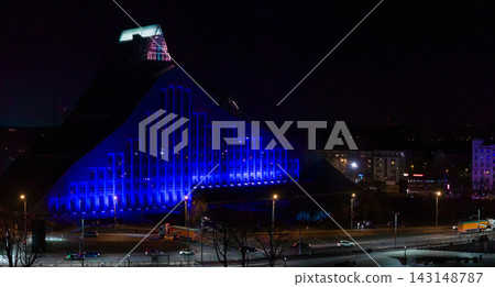 Aerial night view shows the National Library of Latvia in deep blue with a cyan crown by the Daugava embankment in Riga. Cars move and lampposts glow, long exposure. Aerial night view shows the National Library of Latvia in deep blue with a cyan crown by the Daugava embankment in Riga. Cars move and lampposts glow, long exposure. 143148787