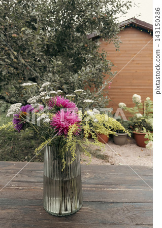 Autumn bouquet of pink asters and goldenrod in glass vase on wooden table Autumn bouquet of pink asters and goldenrod in glass vase on wooden table 143150286
