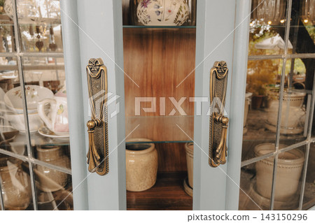 Vintage wooden cabinet with brass handles and glass doors storing ceramic dishware Vintage wooden cabinet with brass handles and glass doors storing ceramic dishware 143150296