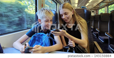 Smiling teenage girl and young boy using smartphones while traveling on a train 143150864