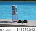 Reusable water bottle and sunglasses placed beside a swimming pool on a sunny day. Summer lifestyle scene featuring hydration and relaxation near clear blue water. 143151042