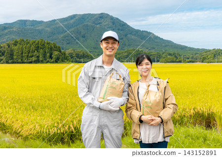 A middle-aged couple holding rice bags in a rice field full of ripened rice. A middle-aged couple holding rice bags in a rice field full of ripened rice. 143152891