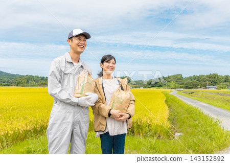 一對中年夫婦手捧米袋,站在滿是成熟稻米的稻田。 一對中年夫婦手捧米袋,站在滿是成熟稻米的稻田。 143152892