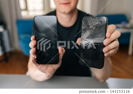 Man holding two smartphones, showing repaired device with clean screen and damaged phone with cracked display, illustrating successful repair service, close-up, cropped shot Man holding two smartphones, showing repaired device with clean screen and damaged phone with cracked display, illustrating successful repair service, close-up, cropped shot 143153116