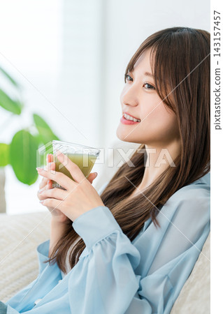 A young woman relaxing on a sofa while sipping a green smoothie. A young woman relaxing on a sofa while sipping a green smoothie. 143157457