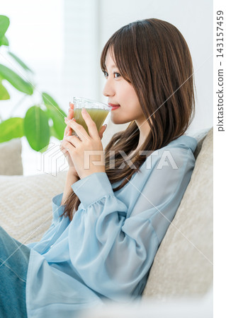 A young woman relaxing on a sofa while sipping a green smoothie. A young woman relaxing on a sofa while sipping a green smoothie. 143157459