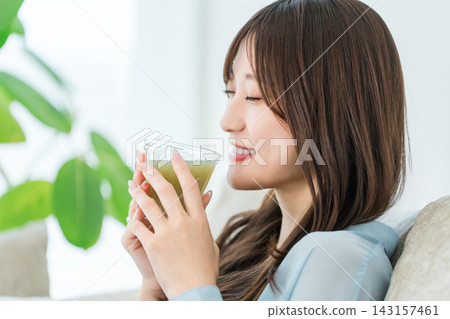 A health-conscious young woman relaxes with a smile on her face, holding a smoothie. A health-conscious young woman relaxes with a smile on her face, holding a smoothie. 143157461