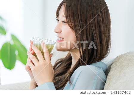 A health-conscious young woman relaxes with a smile on her face, holding a smoothie. A health-conscious young woman relaxes with a smile on her face, holding a smoothie. 143157462