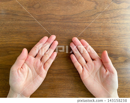A woman's hands, palms visible, on a wooden table. A woman's hands, palms visible, on a wooden table. 143158238