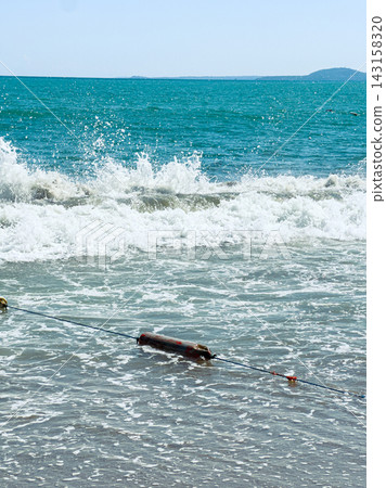 Waves crash on the shore with a wooden object in the water and a distant island on a sunny day Waves crash on the shore with a wooden object in the water and a distant island on a sunny day 143158320
