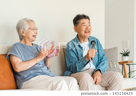 A smiling senior couple enjoying karaoke in their living room. A smiling senior couple enjoying karaoke in their living room. 143158423