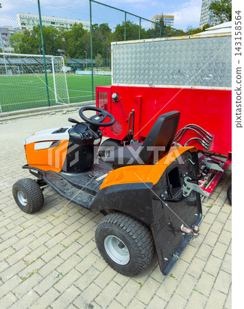 Lawn tractor parked near a sports field on a sunny day in an urban area 143158564