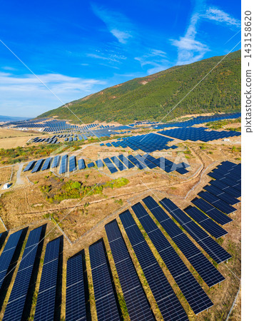 Solar panels cover a large area in a renewable energy site located in a mountainous region under a bright blue sky Solar panels cover a large area in a renewable energy site located in a mountainous region under a bright blue sky 143158620